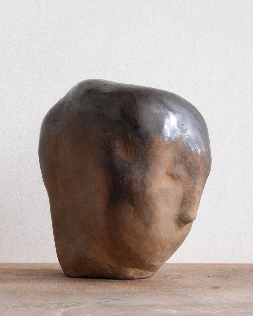 Inbetween Worlds by Arran Gregory, a large burnished clay head with a smoky black crown and warm brown face, turned to the right