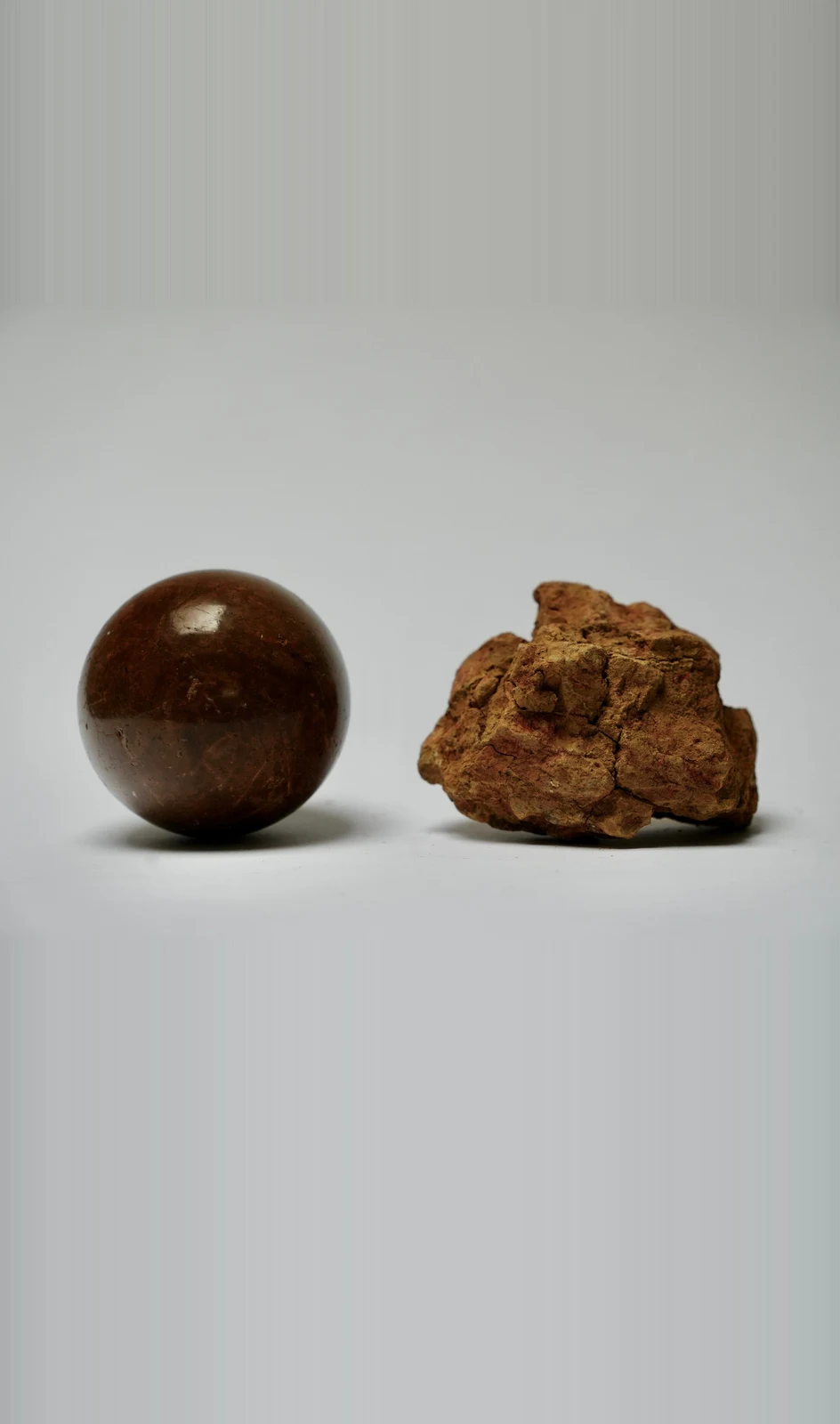 Dorodango Pair I by Edie Evans, a polished clay sphere beside a rough lump of excavated earth