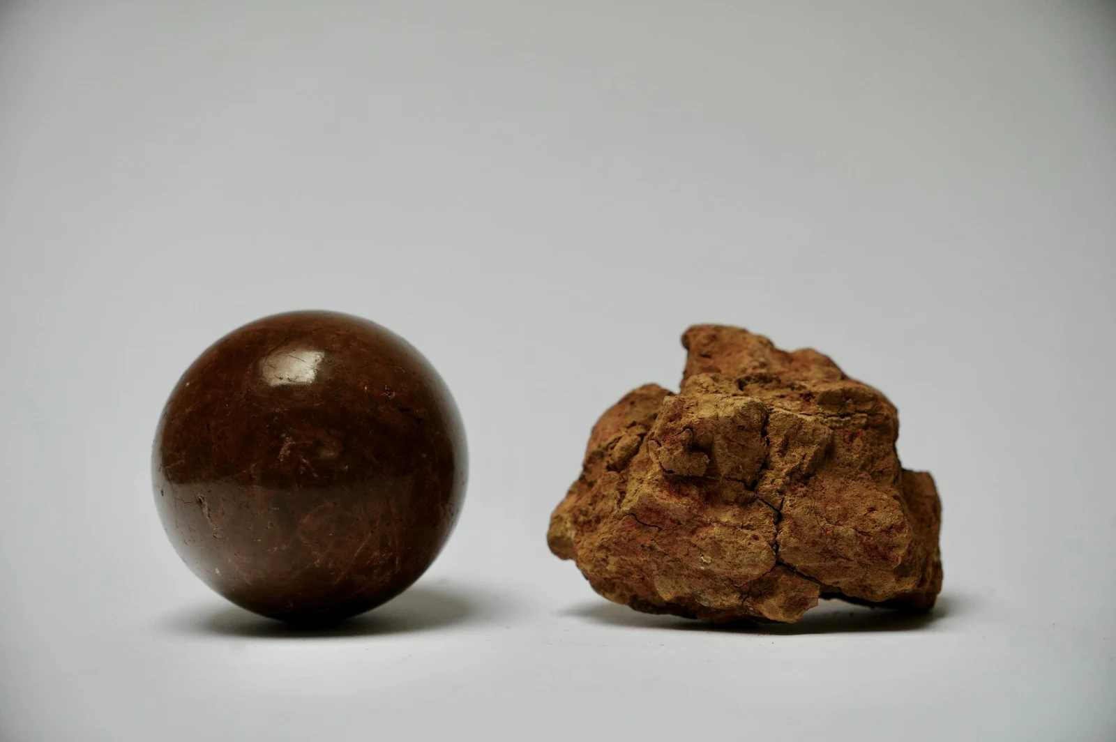 Dorodango Pair I by Edie Evans, a polished clay sphere beside a rough lump of excavated earth