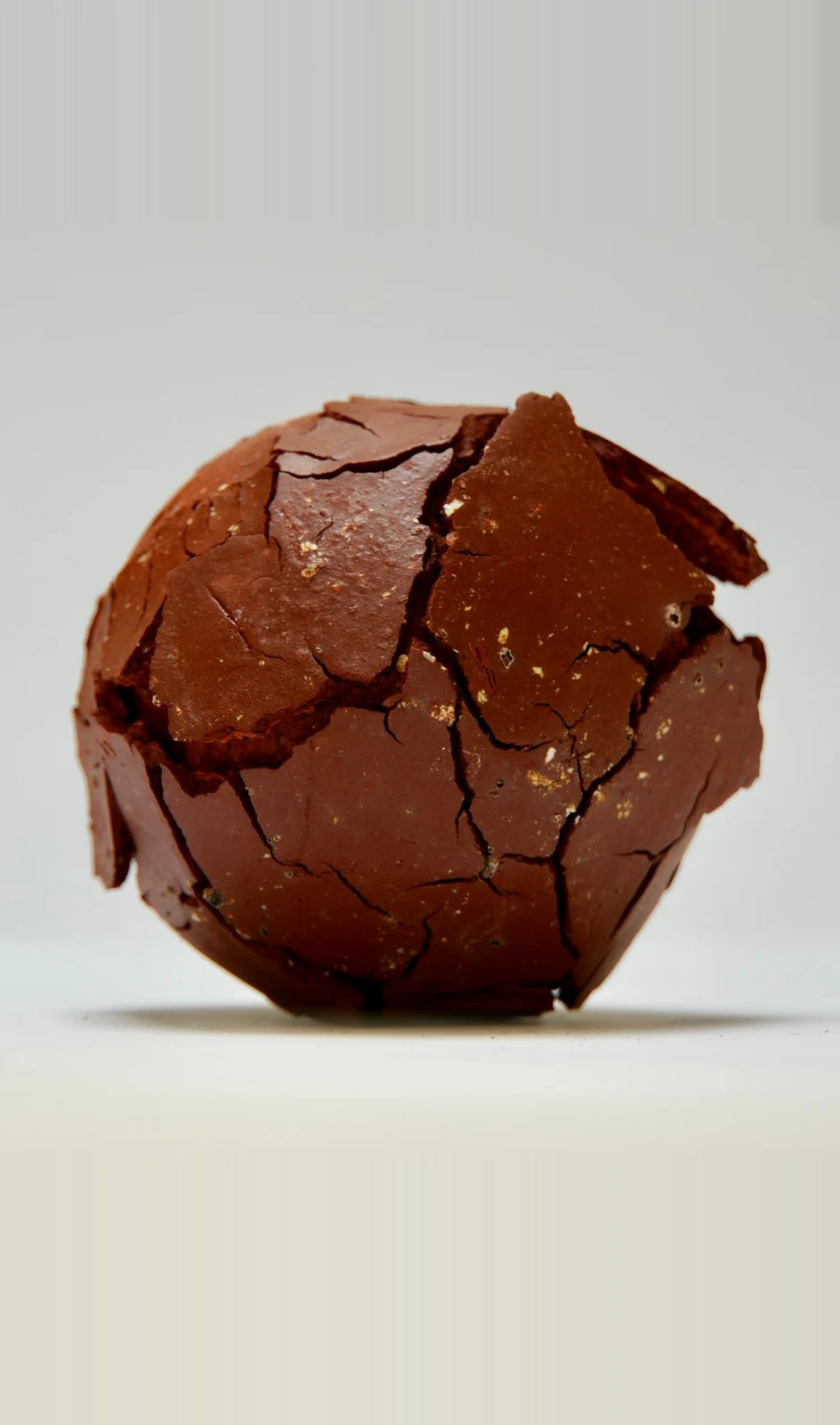 Fragmentation 1 by Edie Evans, a red clay sphere whose cracked surface lifts away in flakes