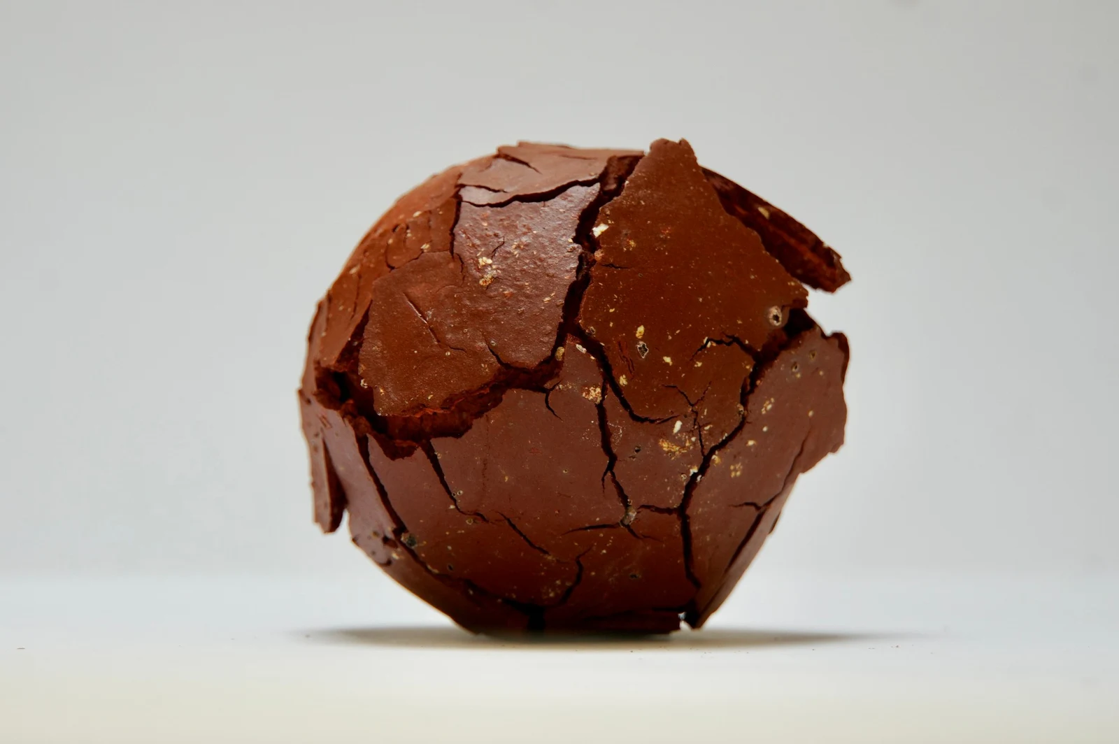 Fragmentation 1 by Edie Evans, a red clay sphere whose cracked surface lifts away in flakes