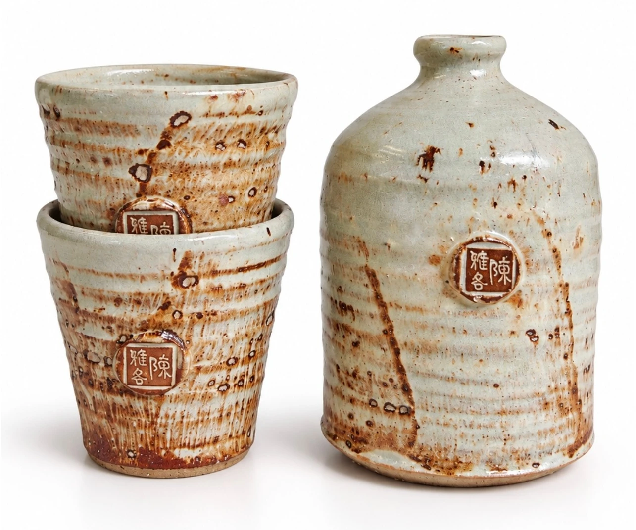 Sake Set #4 by Jacob Chan, two stacked celadon cups with rust flashes beside a pale glazed bottle