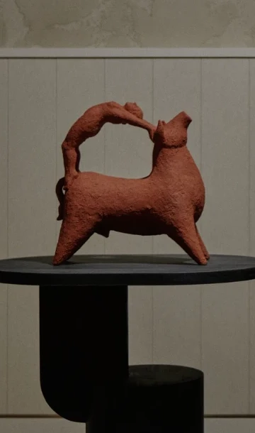 Bull Leaping II by Zahed Tajeddin, a terracotta bull with a figure arching over its back, on a black wooden plinth